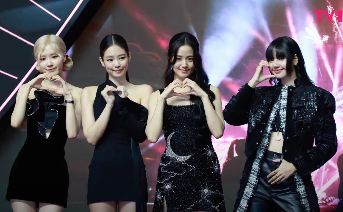 All four BLACKPINK members, ROSÉ, JENNIE, JISOO and LISA, posing with finger hearts on stage at a fan event